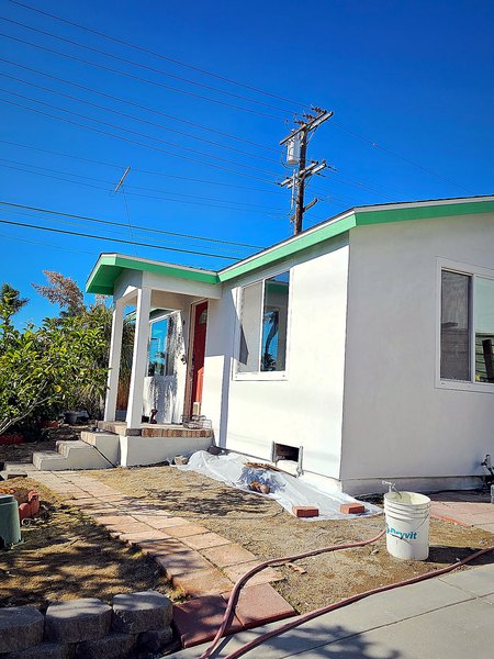 Front of a re-stuccoed home with fresh white walls and original green roof trim.