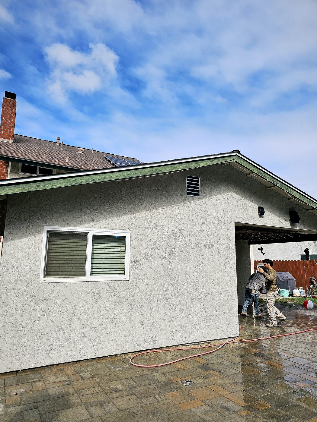 Same side wall finished with smooth white stucco, clean brick chimney and patio visible.