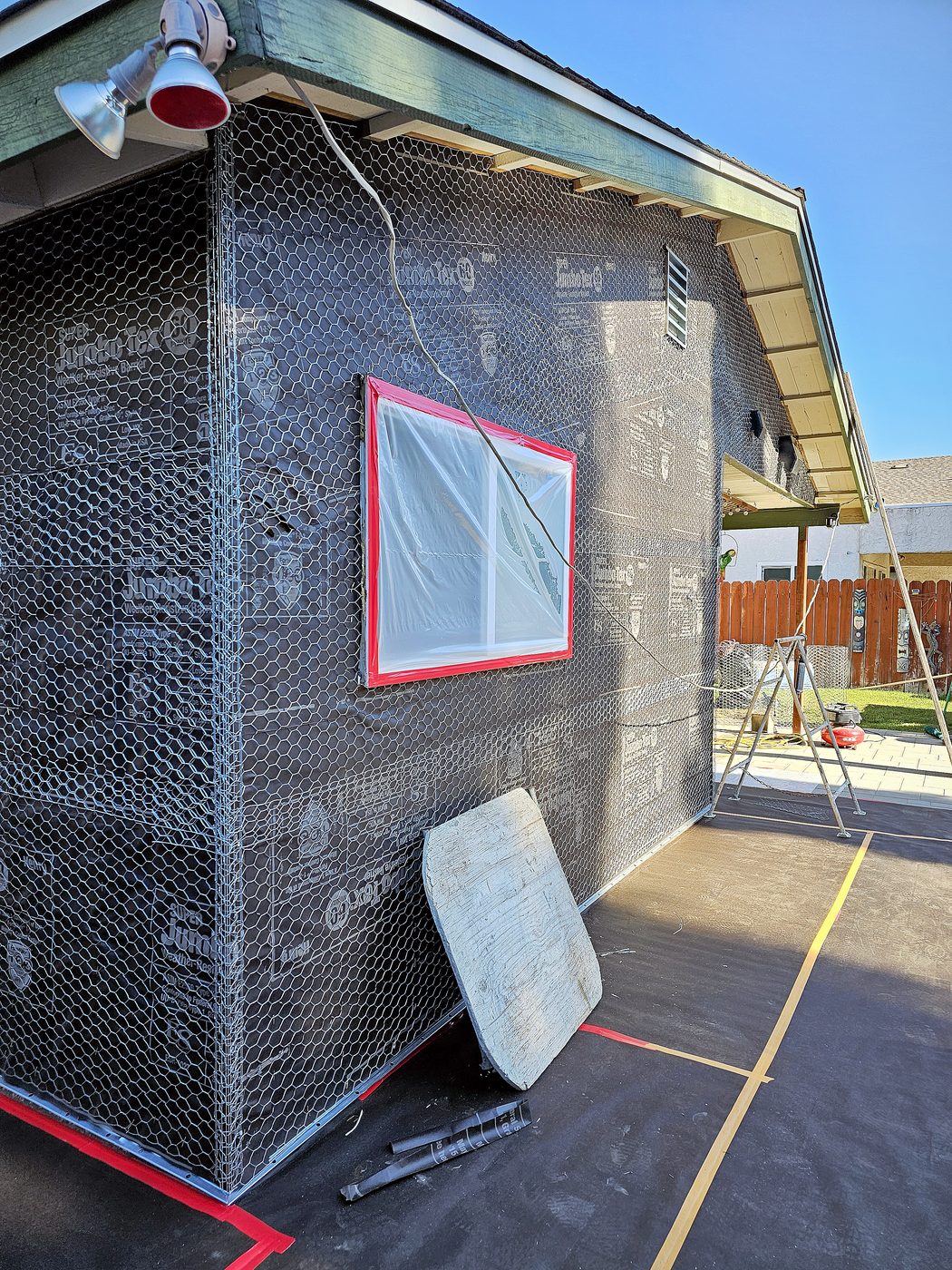 Side wall of a home covered in fresh tar paper and wire lath after old stucco was removed.