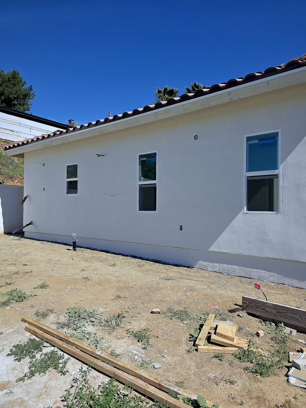 Completed new-construction home with smooth white stucco walls, Spanish tile roof, dirt yard ready for landscaping.