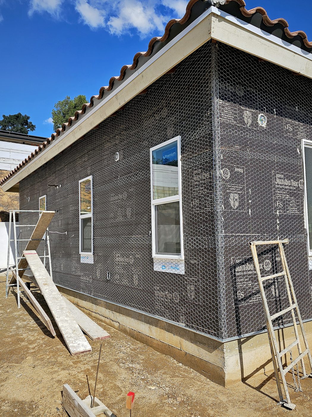 Side wall of a new-construction home with paper and wire lath installed under a Spanish clay-tile roof, ready for stucco.