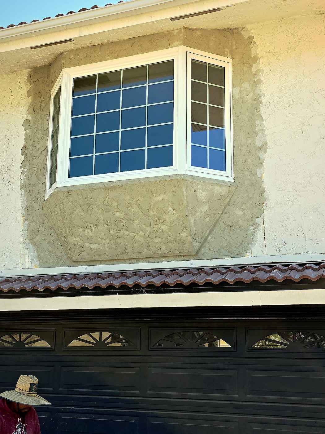 Same bay window with fresh scratch-coat stucco applied around it, scaffolding removed, clean window return.