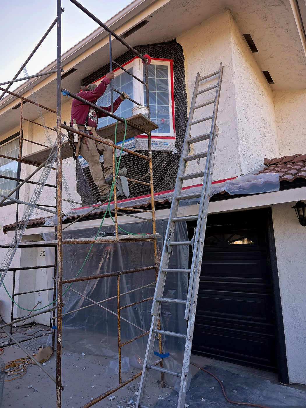 Two-story San Diego home with scaffolding set up around a bay window, wire lath in place, ready for stucco.