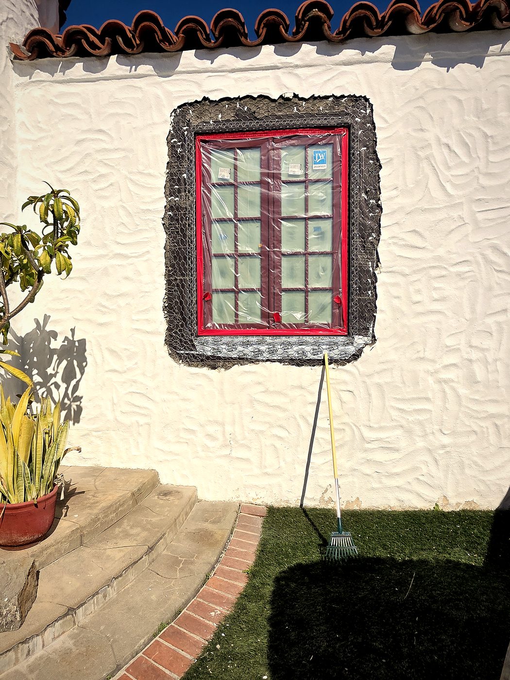 Window on a 1920s Spanish home, surrounded by dark wire lath after damaged stucco has been removed.